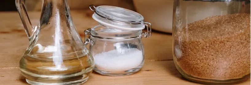 Glass jars of oil, salt and brown sugar on a wooden table